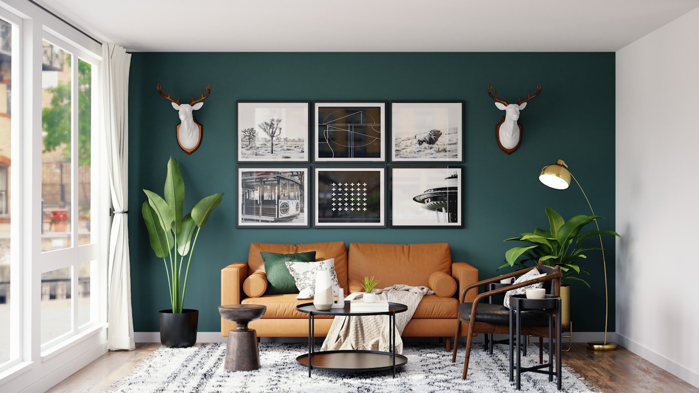 Living room with a tan leather sofa against a deep green wall with framed art
